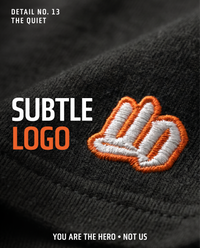 Close-up of subtle orange and white UndrDog logo embroidered near the hem of an UndrDog Midnight black hemp T-shirt.